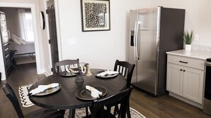 Une cuisine moderne avec une table à manger pour quatre personnes, un réfrigérateur en acier inoxydable et une œuvre d’art encadrée accrochée au mur.