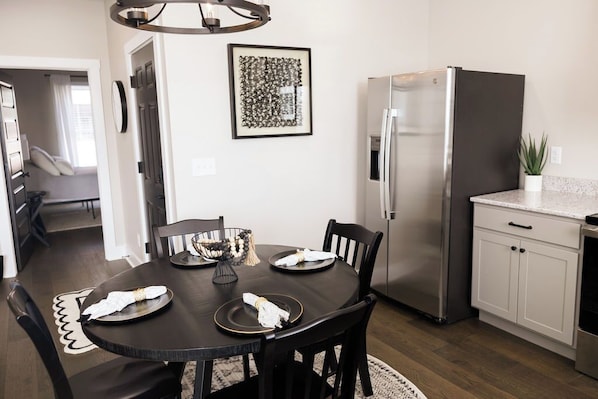 Une cuisine moderne avec une table à manger pour quatre personnes, un réfrigérateur en acier inoxydable et une œuvre d’art encadrée accrochée au mur.