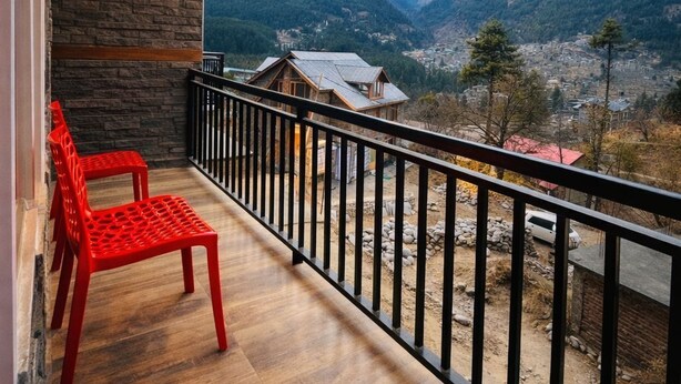 A balcony with a wooden floor, two red chairs, and a view of snow-capped mountains. - North Star Manali (Manali)