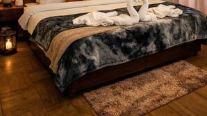 A neatly made bed with a dark patterned bedspread, a wooden headboard, and two wall-mounted lamps. - North Star Manali (Manali)