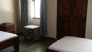 Een slaapkamer met twee bedden, een klein nachtkastje, een kledingkast en een raam met gordijnen.