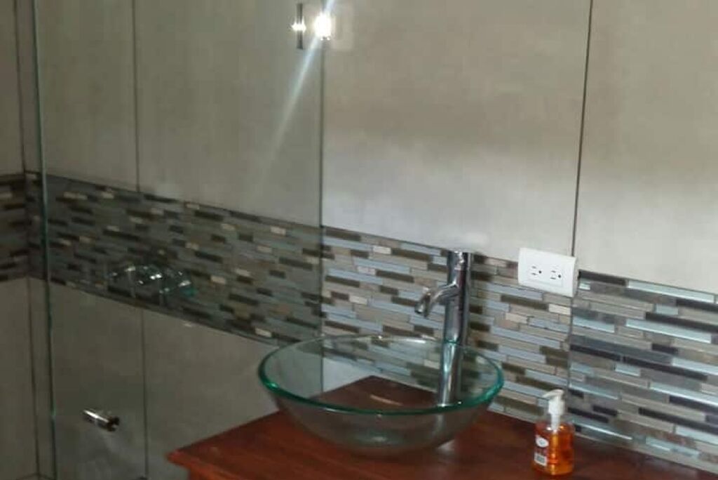 A modern bathroom with a glass bowl sink, a wooden countertop, and a tiled backsplash.