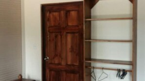 Een kamer met een houten deur, een klein tafeltje en een wandplank met kapstokken.