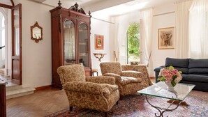 Una sala de estar con un mueble de madera grande, un sofá, sillones estampados y una mesa de centro de vidrio.