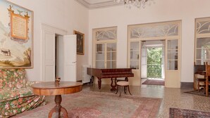 Una habitación con un piano, una mesa redonda de madera, un sofá floral y un cuadro grande en la pared.