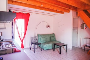 Ein Wohnzimmer mit einem grünen Sofa, einem kleinen Tisch, einem Sessel und einer Küchenzeile mit Spüle und Herd.