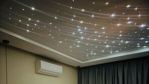 Ein Hotelzimmer mit einem ordentlich bezogenen Bett, einem Nachttisch, einer Wand-Klimaanlage und einer Decke mit Lichterketten.