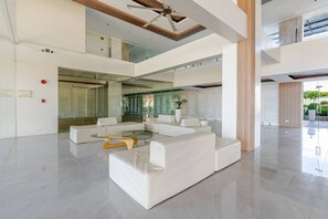 A spacious, modern lobby with a high ceiling, a glass elevator, and a seating area with white sofas and a glass coffee table. - Cozy and Nature-inspired Studio Unit (Lapu-Lapu)