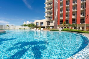 A swimming pool with a tiled edge, surrounded by a building with balconies and a clear sky. - Cozy and Nature-inspired Studio Unit (Lapu-Lapu)