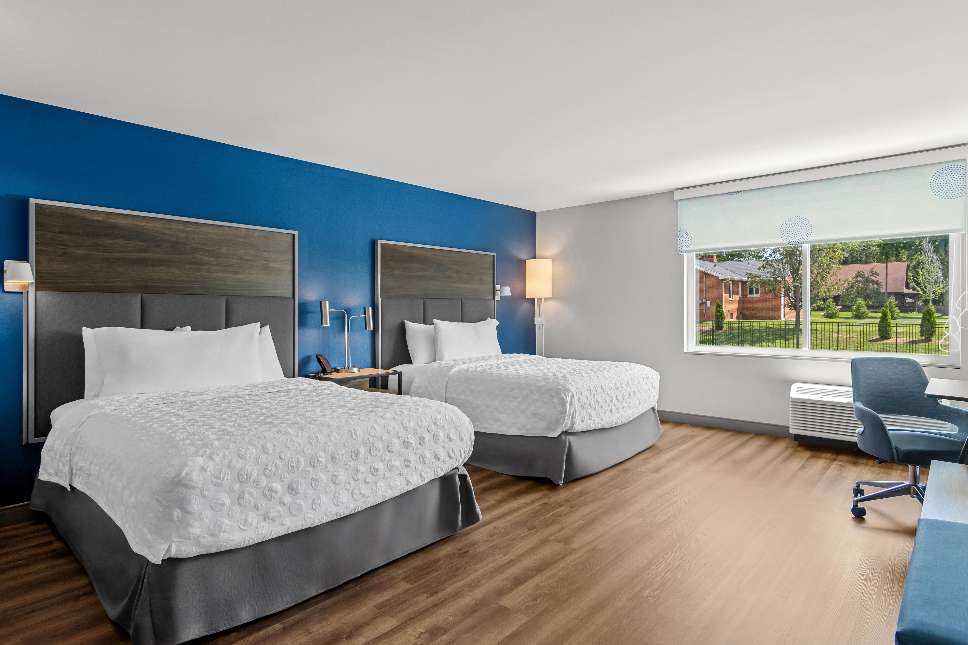 Une chambre d’hôtel avec deux lits, un bureau et une grande fenêtre donnant sur l’extérieur.