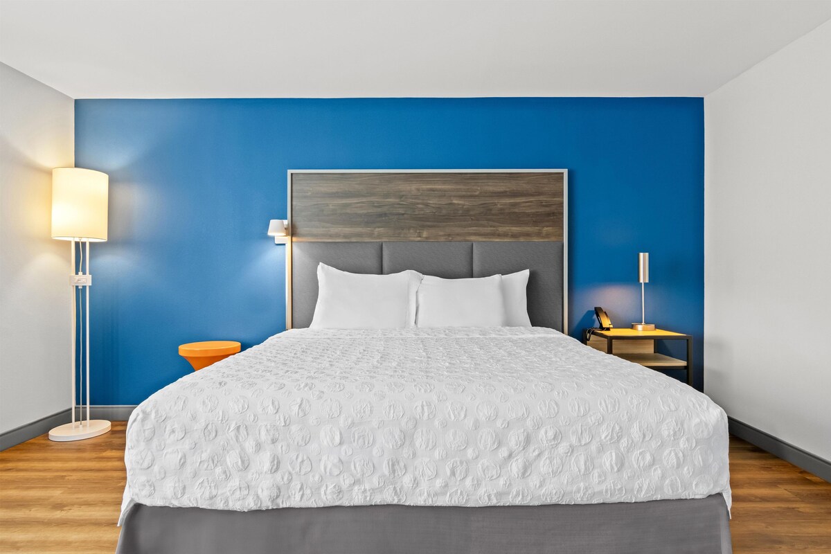 A hotel room with a large bed, a nightstand, a lamp, and a blue accent wall.