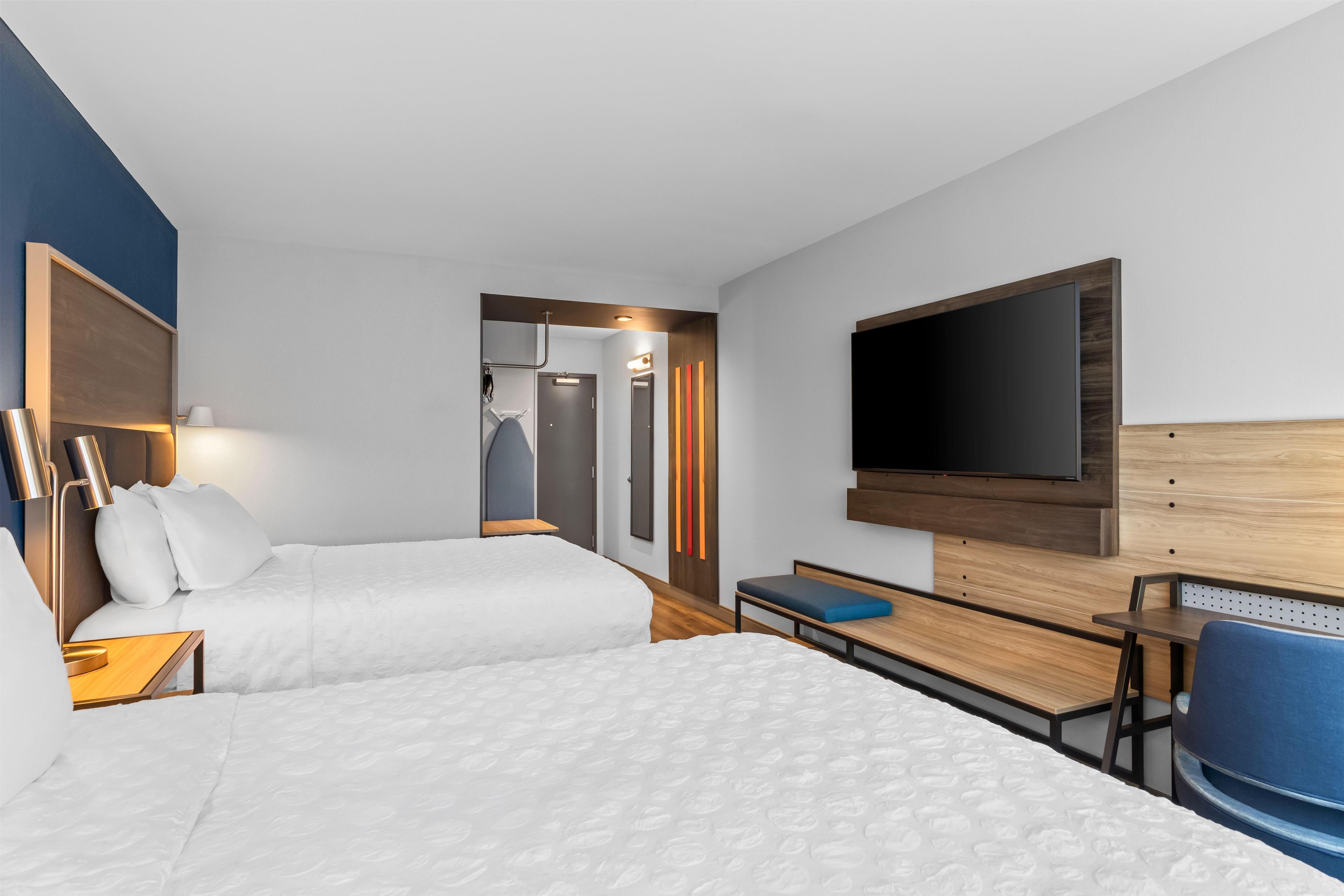 Una habitación de hotel con dos camas, un escritorio, una silla, un televisor y un armario.