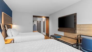 Una habitación de hotel con dos camas, un escritorio, una silla, un televisor y un armario.