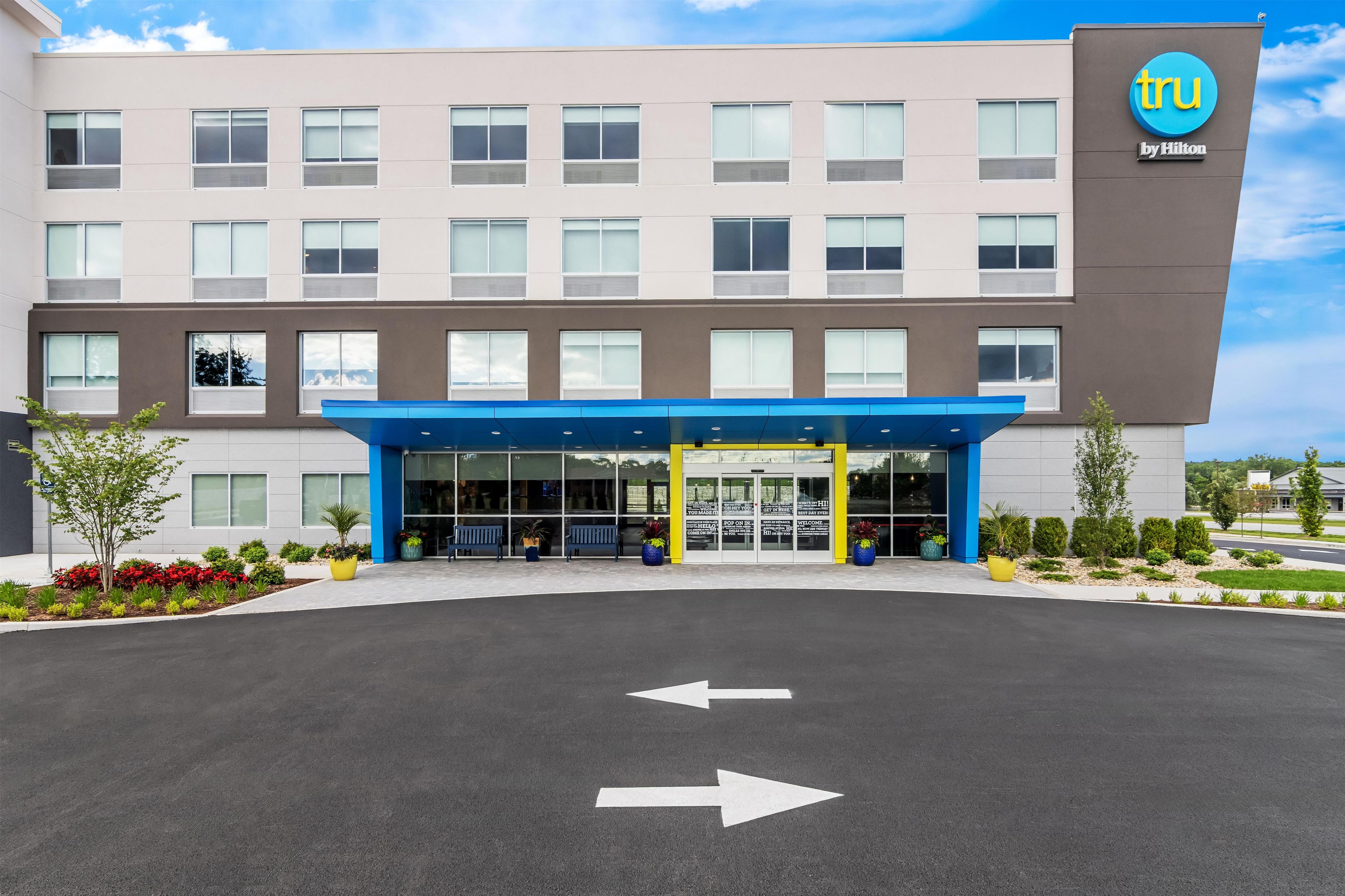 A modern hotel building with a blue entrance canopy, a clear sky, and directional arrows on the pavement.