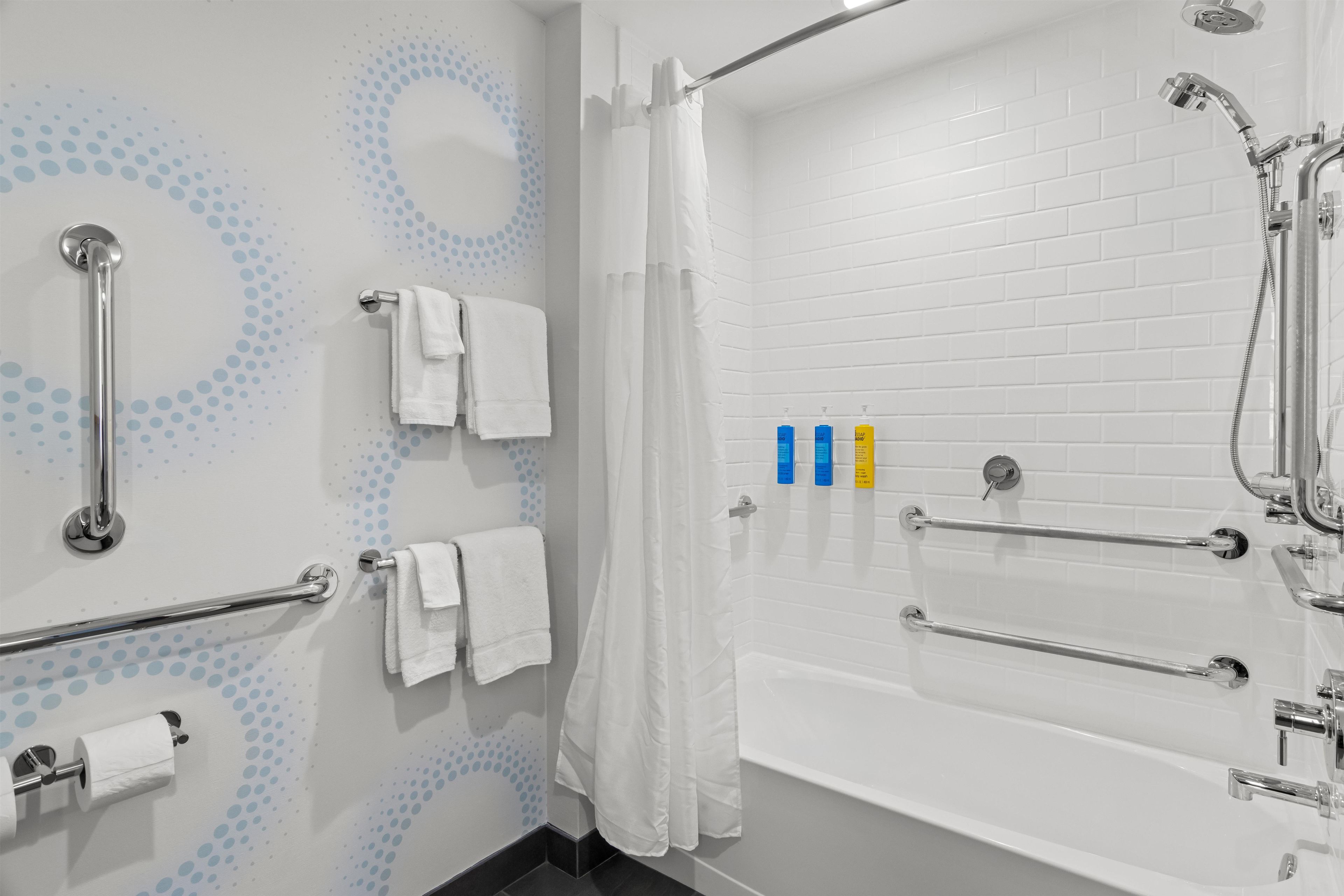 A modern bathroom with a white bathtub, grab bars, a showerhead, and a toilet paper holder.