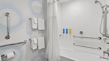 A modern bathroom with a white bathtub, grab bars, a showerhead, and a toilet paper holder.