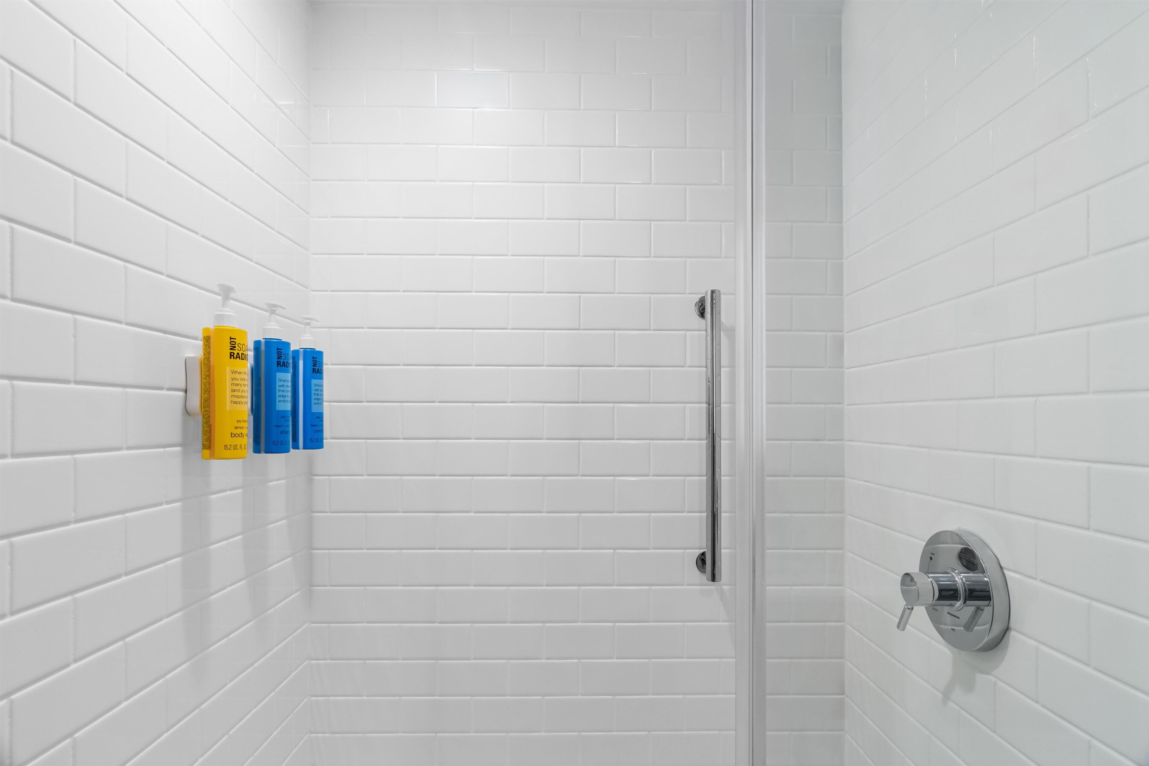 Un baño con azulejos blancos tipo metro, cerramiento de ducha de vidrio y secamanos montado en la pared.