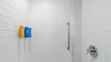 Une salle de bain avec des carreaux de céramique blancs rectangulaires, une douche en verre et un sèche-mains fixé au mur.