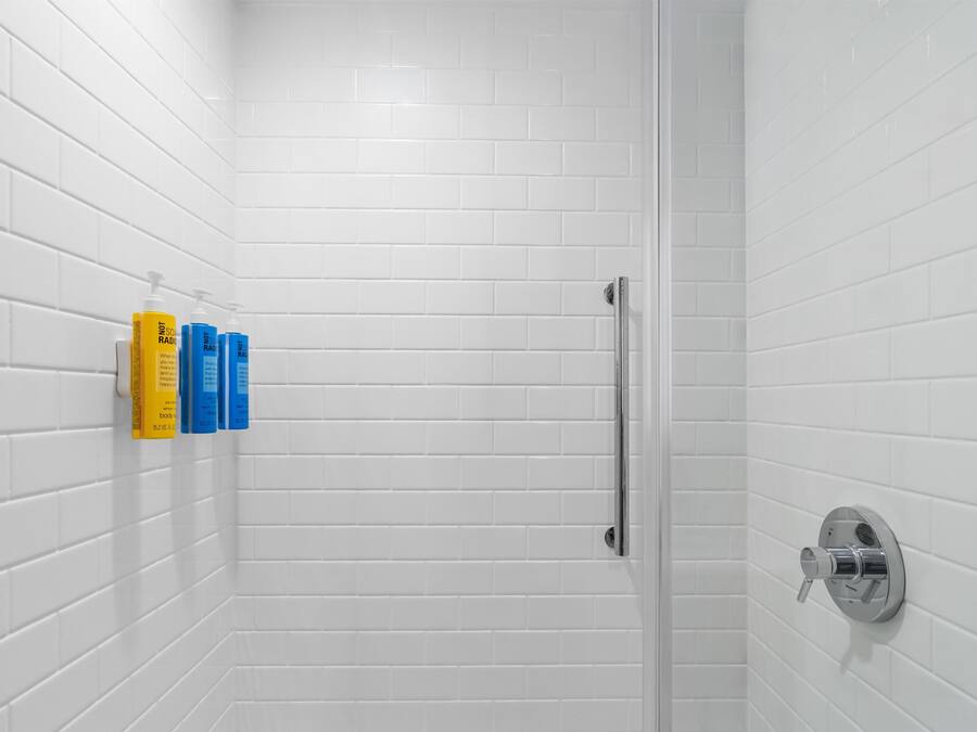 Une salle de bain avec des carreaux de céramique blancs rectangulaires, une douche en verre et un sèche-mains fixé au mur.