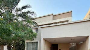 Un edificio moderno con un área de entrada empavedada, una palmera y un pequeño jardín.