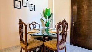 A dining area with a glass table surrounded by four wooden chairs with cushioned seats.