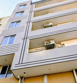 Ein modernes Gebäude mit mehreren Balkonen, Klimaanlagen und einer sauberen, geometrischen Fassade.