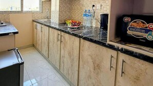 A kitchen with light-colored cabinets, a tiled backsplash, and a black countertop. There is a box of Haier brand appliances on the counter.