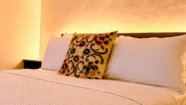 A neatly made bed with a patterned pillow and a plain pillow, a white textured blanket, and a wooden headboard.