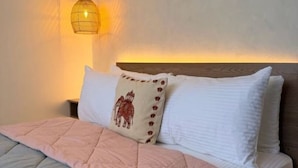 Un letto rifatto con un copriletto rosa e grigio, una testiera in legno e una lampada fissata al muro.