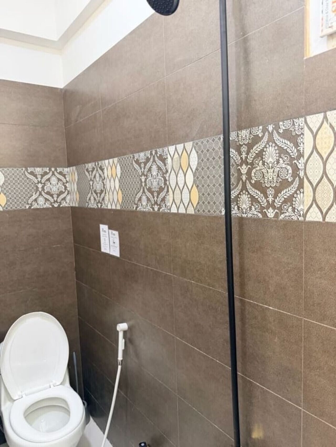 Une salle de bain comprenant des toilettes, un espace douche et des carreaux décorés.