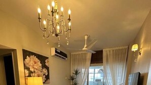 A living room with a chandelier, a sofa, a coffee table, a TV, and a painting on the wall. - Oceanfront Oasis by Jannat Vacation Rentals (Karachi)