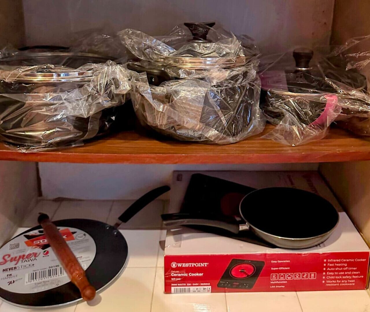 A kitchen shelf with cookware, including a pan and a box of a ceramic cooker.
