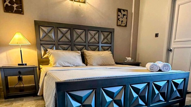 A bedroom with a bed, bedside tables, a wall-mounted light fixture, and artwork on the walls. - Oceanfront Oasis by Jannat Vacation Rentals (Karachi)