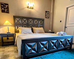 A bedroom with a bed, bedside tables, a wall-mounted light fixture, and artwork on the walls.