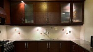 A kitchen with dark wooden cabinets, a tiled backsplash, and a single pendant light. - Oceanfront Oasis by Jannat Vacation Rentals (Karachi)