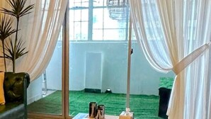 A room with a sliding glass door leading to a balcony with a green floor, a hanging light fixture, and a small table with items on it. - Oceanfront Oasis by Jannat Vacation Rentals (Karachi)