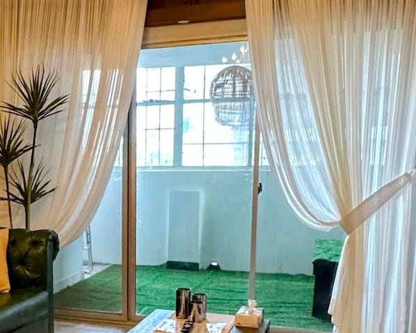 A room with a sliding glass door leading to a balcony with a green floor, a hanging light fixture, and a small table with items on it.