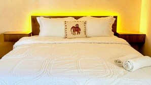 A neatly made bed with a white bedspread and pillows, a rolled towel, and a bedside lamp. - Gourmet Getaway One by Jannat Vacation Rentals (Karachi)