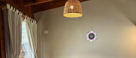A room with two white armchairs, a wooden table, a woven pendant light, a wall clock, and a window with curtains.