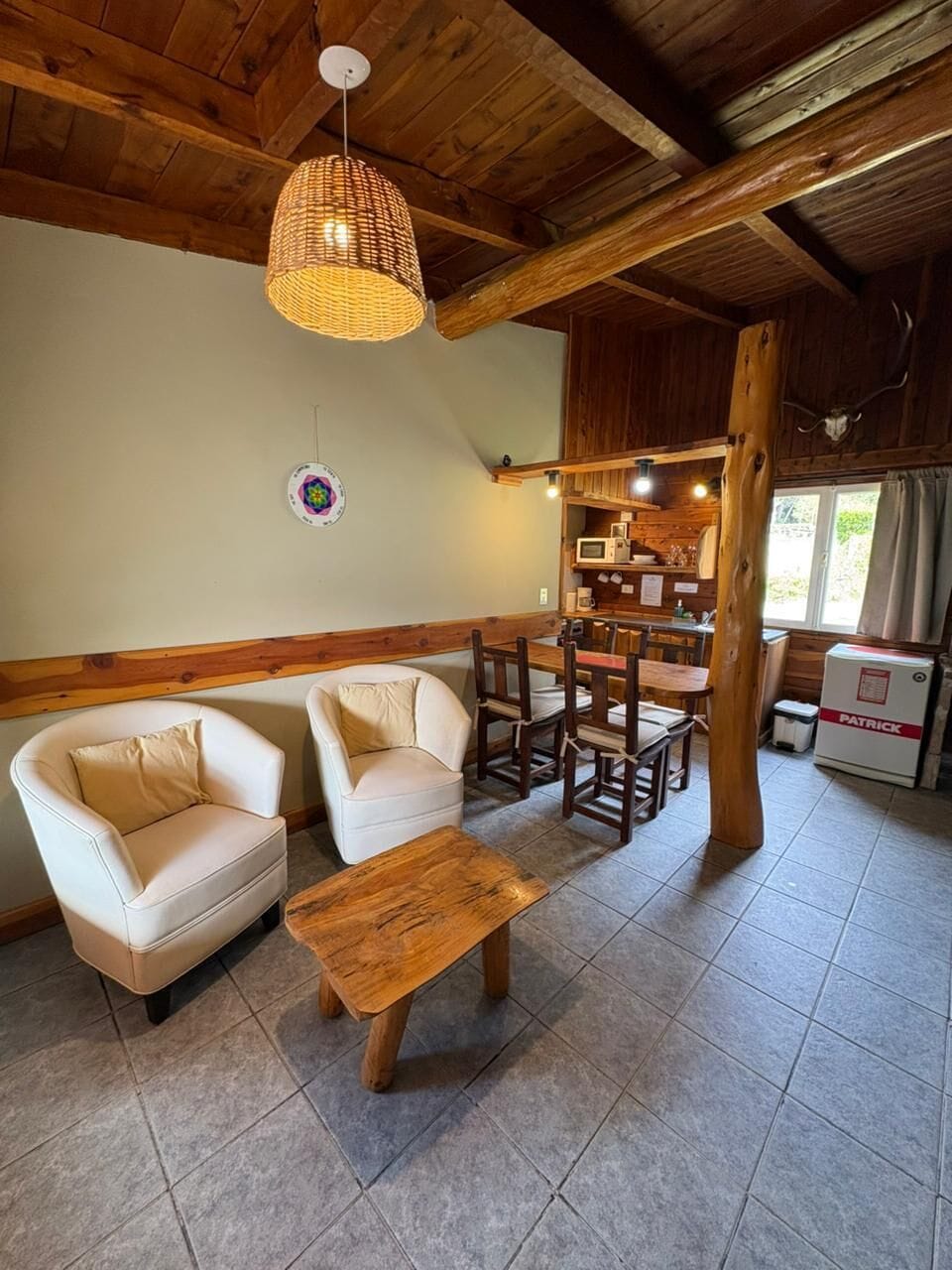 Una habitación acogedora con techo de madera, una mesa de comedor con sillas, un sofá y una pequeña cocina con refrigerador.