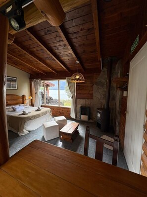 A wooden cabin interior with a bed, seating area, and a fireplace. - Cabañas Walnor (Villa Traful)