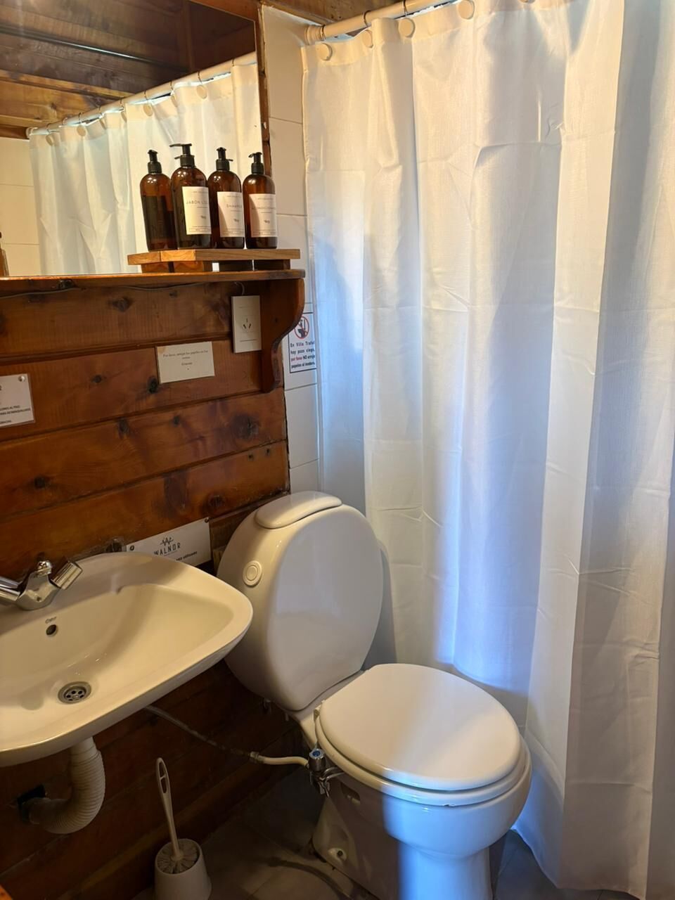 Kylpyhuone, jossa on puinen seinä, valkoinen pesuallas, wc ja suihkuverho.
