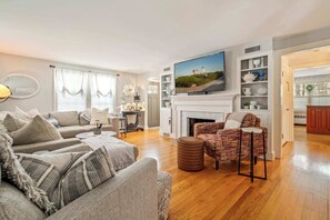 A living room with a fireplace, a television mounted above it, and a dining area visible through an open door. - 5-Bed, Pet-Friendly, Game Room (York)