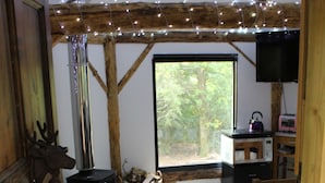 A cozy room with a fireplace, a sofa, a bed, and a window with a view of greenery. - Magical Treehouse/Cabin hidden in Ancient Woodland (Farnham)