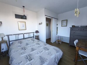 A bedroom with a bed, a desk, a chair, a dresser, and a door leading to another room. - Le Sauze: Bright 60m² Flat near Slopes (Enchastrayes)