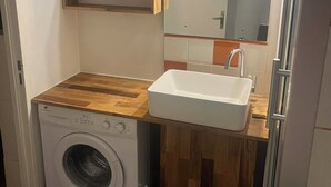 Ett litet och praktiskt tvättrum med tvättmaskin, handfat, hyllor i trä och en spegel.