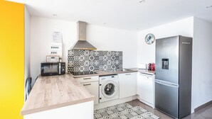 Eine moderne Küche mit einem Edelstahl-Kühlschrank, einer Mikrowelle, einer Waschmaschine und einer strukturierten Spritzschutzwand.