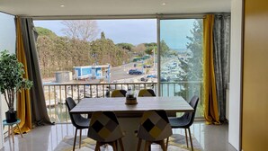 Ein moderner Essbereich mit großem Tisch und Stühlen, einer Topfpflanze und Blick auf eine Marina mit Booten und einer Straße.
