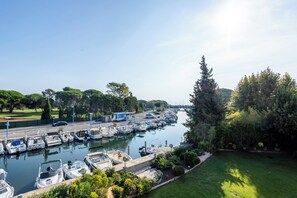 Un port de plaisance où des bateaux sont amarrés le long d’une promenade en bord de mer, entouré de verdure et d’arbres.