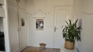 A hallway with a white door, a poster on the wall, a plant on a table, and a woven mat on the floor. - Spacious apartment near Père Lachaise (Paris)